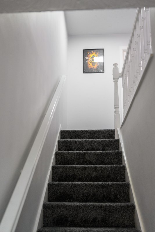 Staircase with dark grey carpet, white walls, handrail and framed artwork