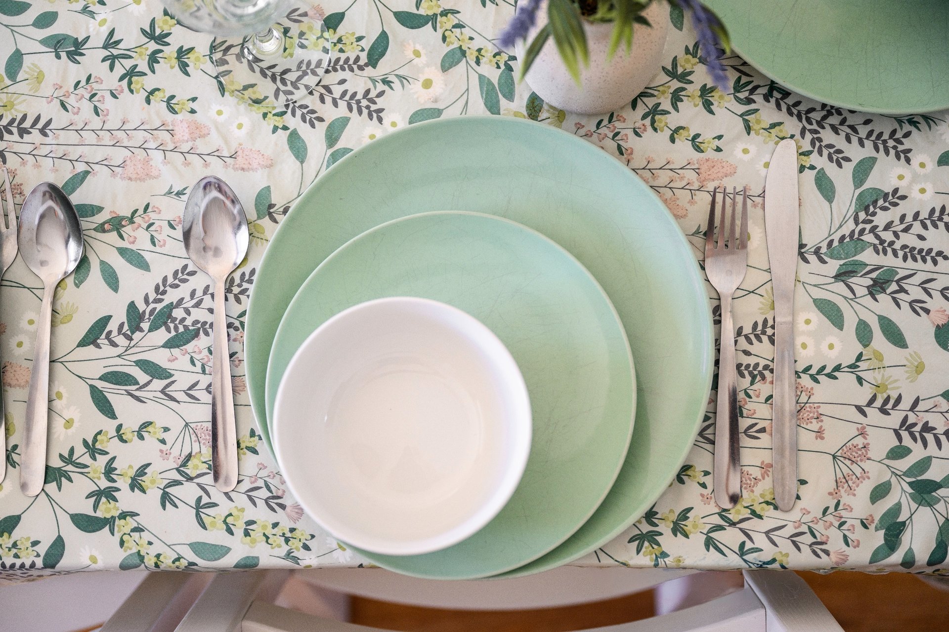 Table setting with stacked green and white plates, cutlery, and botanical patterned tablecloth