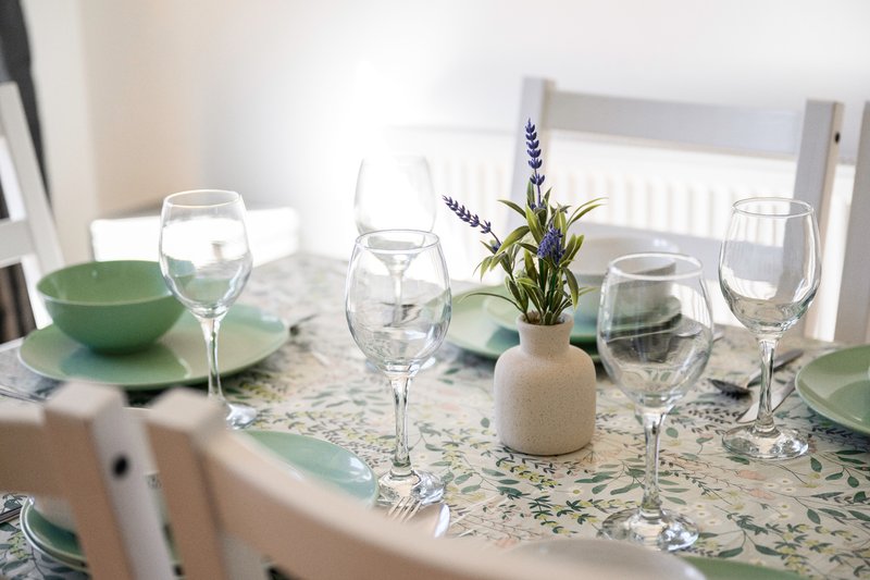 Dining table set with glasses, green bowls, potted plant centerpiece and white tablecloth