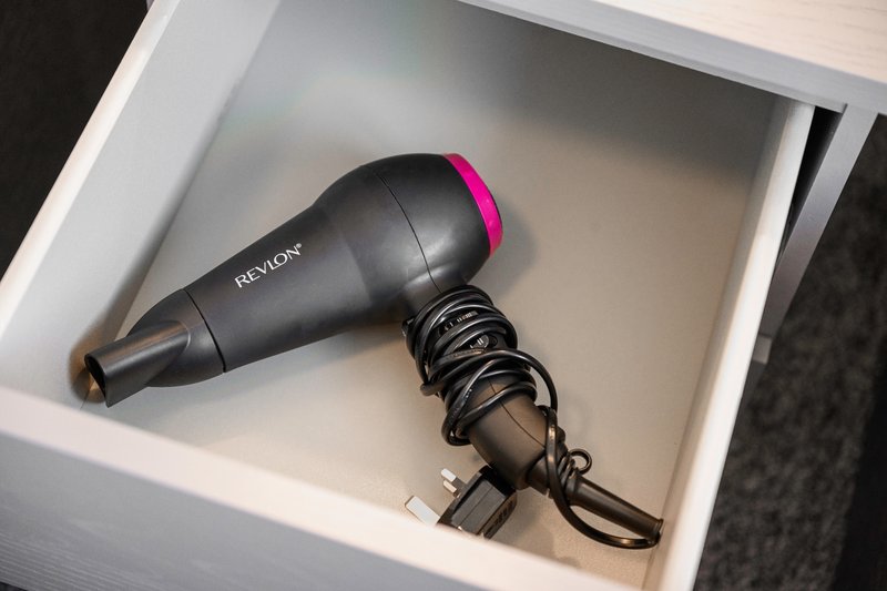 Black and pink hair dryer with cord coiled in white drawer