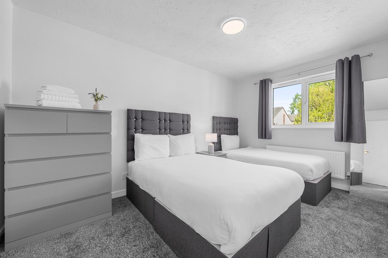 Bright twin bedroom with two double beds, grey headboards, dresser and window with garden view