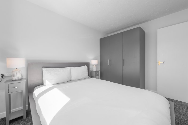 Modern bedroom with double bed, grey headboard, white bedding, and built-in wardrobe