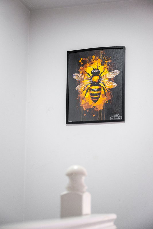 White wall with framed bee artwork and white sculptural object on shelf below