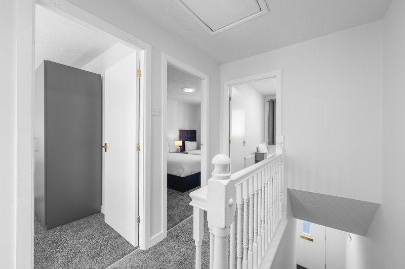 Bright hallway with white walls, gray carpet, open doors leading to bedroom and bathroom
