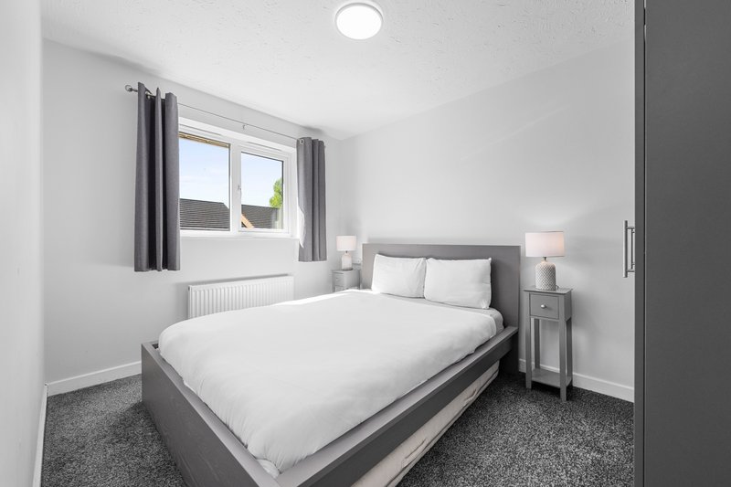 Modern bedroom with grey upholstered bed, white bedding, grey curtains and bedside lamps