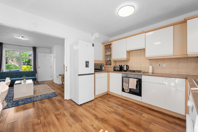 Modern kitchen with white cabinets, wooden floor, and open-plan living area with garden view