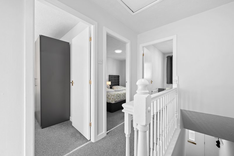 Hallway with white walls, gray carpet, open doors to bedroom and bathroom