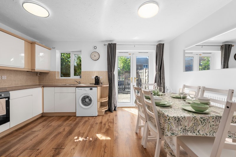 Open-plan kitchen and dining area with white cabinetry, wooden flooring, granite countertop and seating for six.