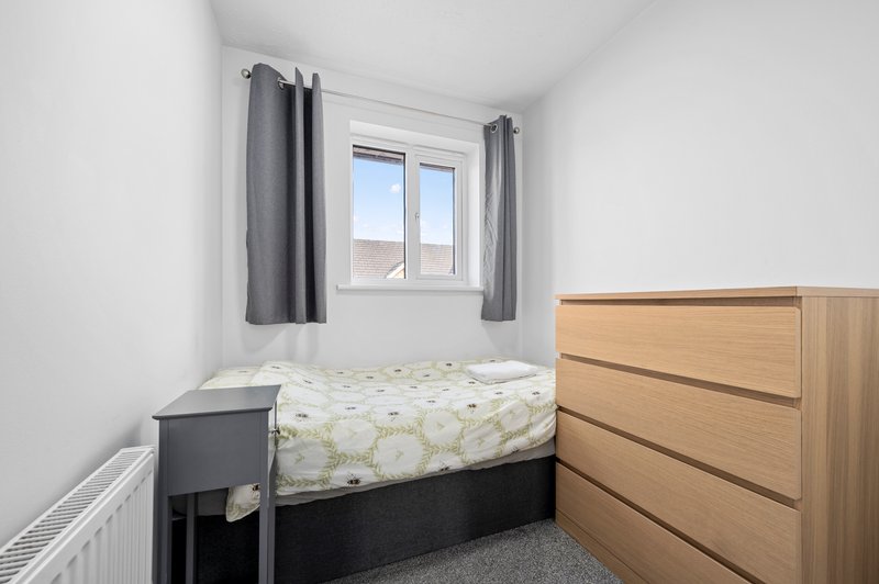 Small bedroom with double bed, wooden dresser, gray curtains and window