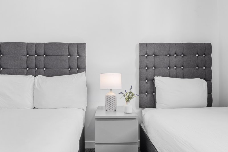 Twin beds with gray upholstered headboards, white bedding, and shared nightstand with lamp