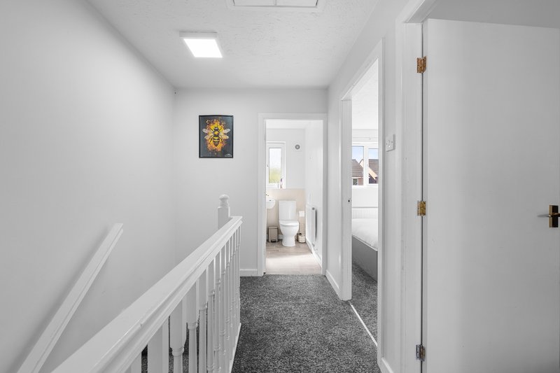 Bright hallway with white walls, railing, grey carpet, and doors leading to rooms