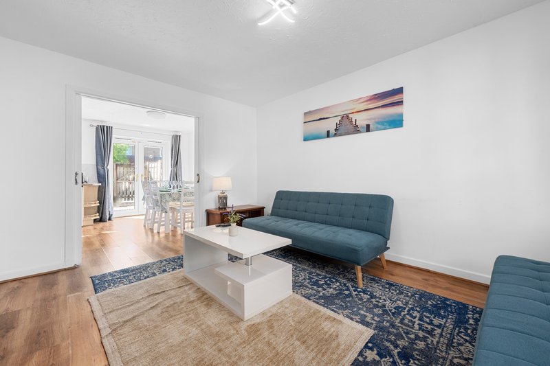 Bright living room with blue sofa, white coffee table, wooden flooring and open doorway to kitchen area