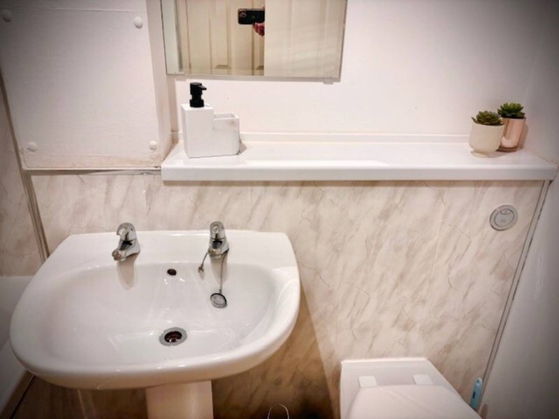Clean bathroom with pedestal sink, mirror, toilet and tiled walls