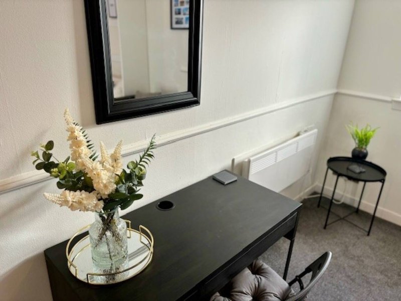 Compact home office with black desk, framed mirror, flowers in vase, and small plant on side table