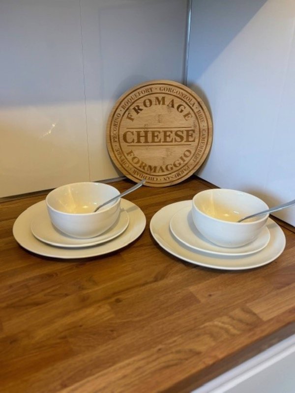 Kitchen shelf with stacked white bowls and plates, wooden cheese board with label