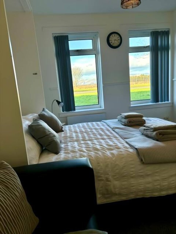 Bright bedroom with double bed, pillows, folded towels, wall clock, and countryside views through windows