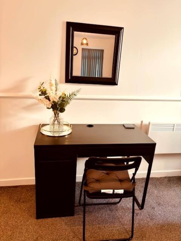 Modern desk with chair, vase of flowers, framed mirror and radiator on wall