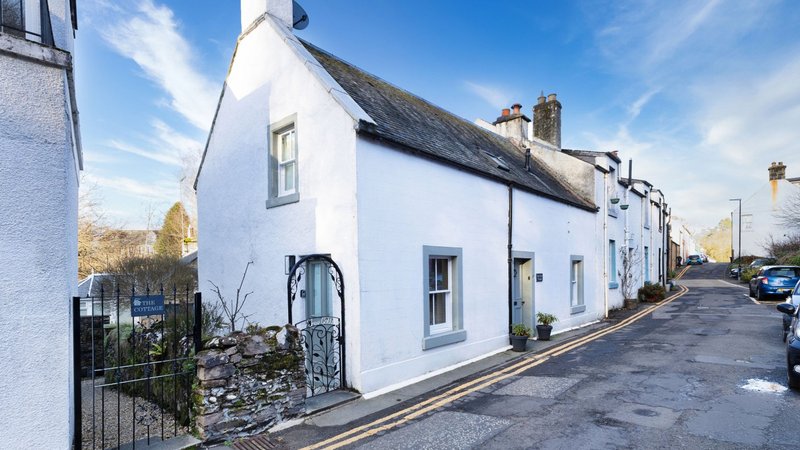 White-painted cottage with thatched roof, black gate and front entrance on quiet street