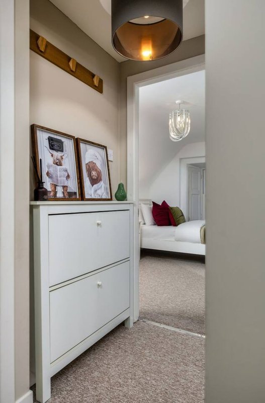 Hallway with white shoe cabinet, framed wall art, pendant lighting and view into bedroom