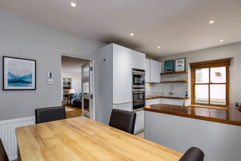Modern kitchen-diner with wooden table, white cabinetry, integrated appliances and window seating