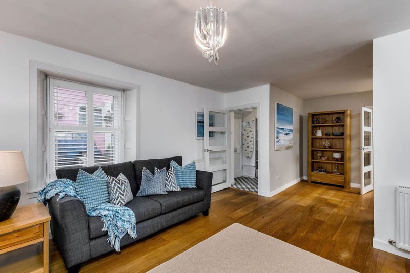 Bright living room with dark sofa, wooden flooring, blue cushions and throws, pendant light