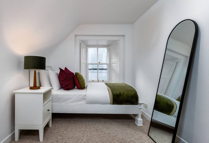 Bright attic bedroom with white bed, burgundy pillows, wooden nightstand, and standing mirror