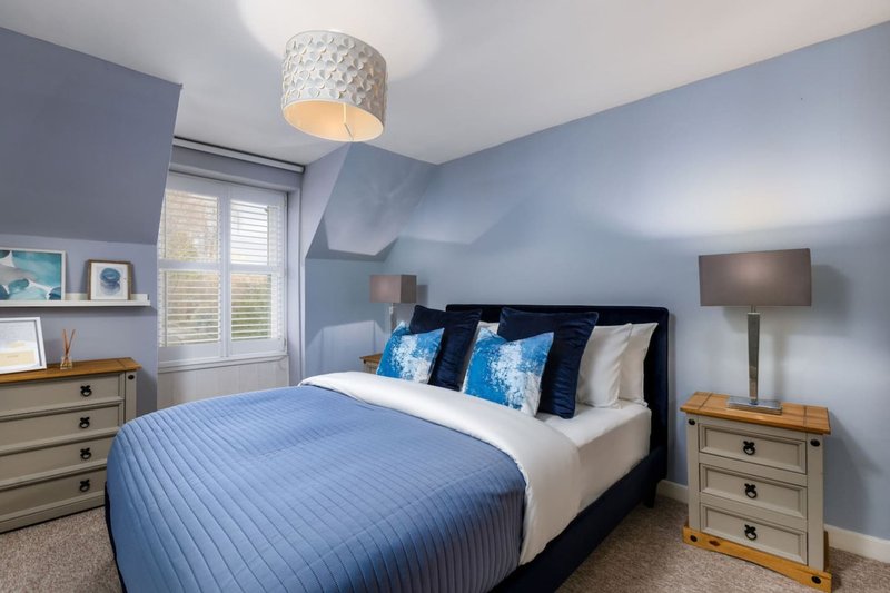 Modern bedroom with blue walls, black bed frame, blue and white bedding, wooden nightstands and lamp