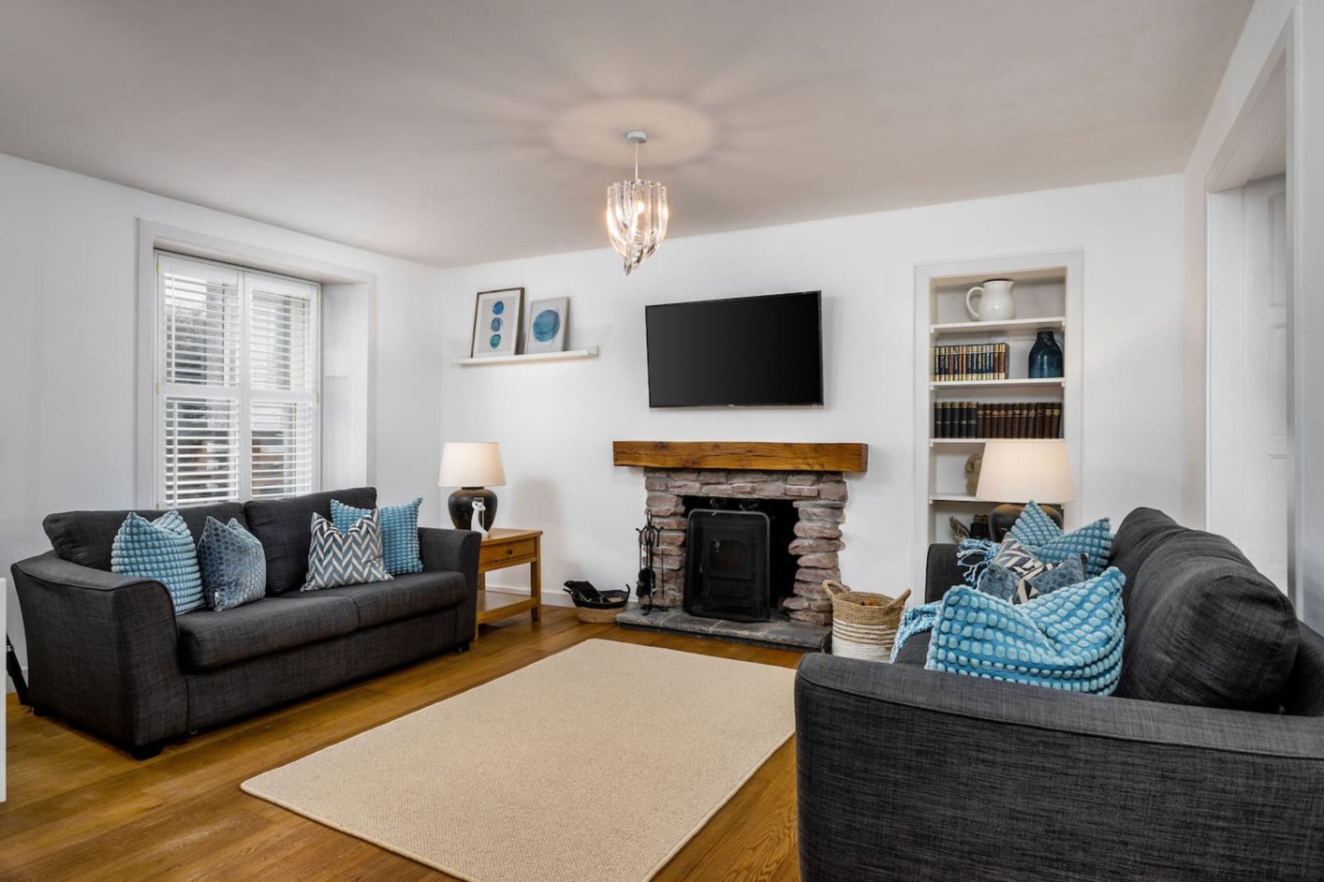 Bright living room with two dark sofas, fireplace, TV, wooden floor and blue cushions