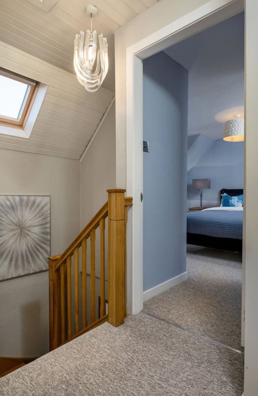 Hallway with wooden staircase, pendant light, and open doorway to bedroom