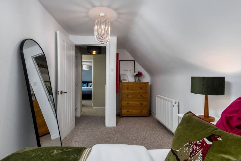 Bright attic bedroom with sloped ceilings, pendant light, wooden chest, mirror and green upholstered furniture