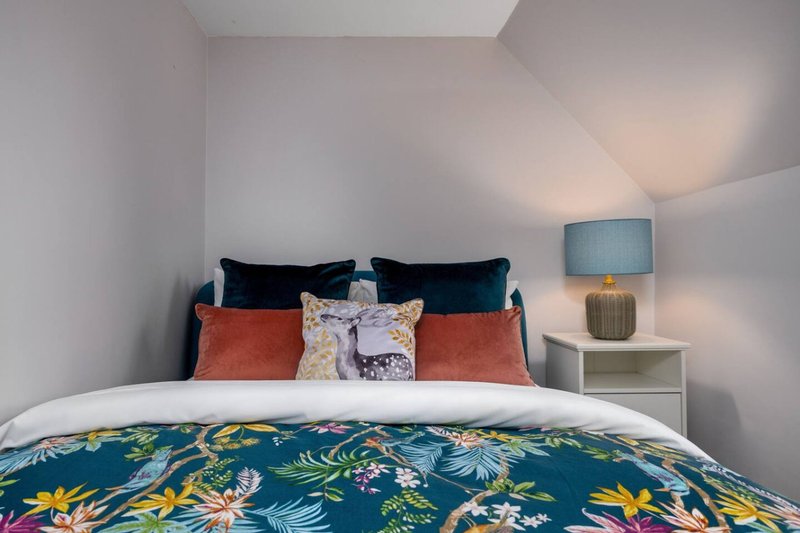Bedroom with double bed, colorful floral bedding, decorative pillows, and bedside lamp