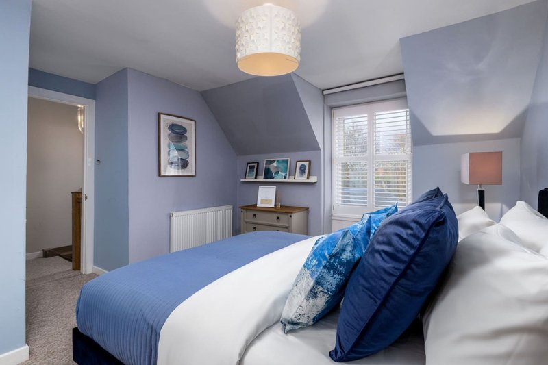 Modern bedroom with double bed, blue pillows, pendant light and shuttered window