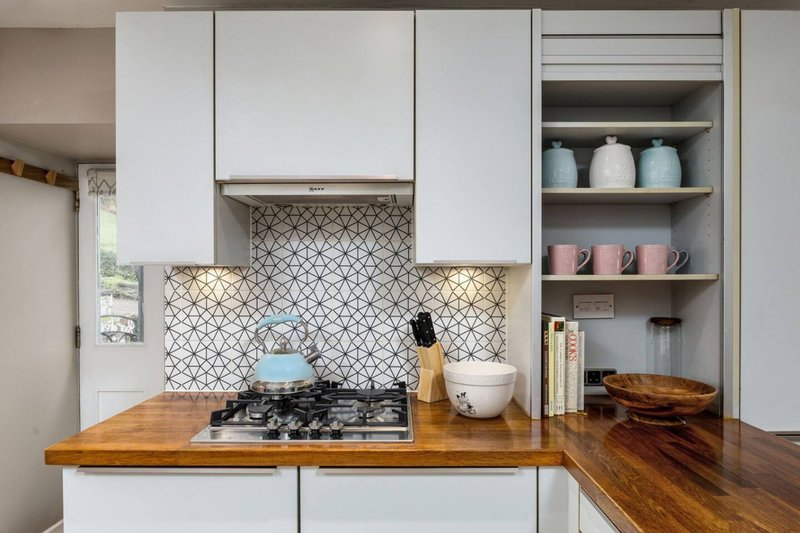 Modern kitchen with white cabinetry, wooden countertop, gas cooktop, and patterned backtile