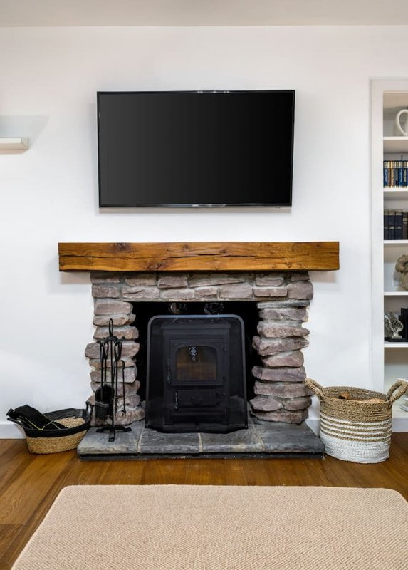 Living room with wall-mounted TV above stone fireplace with wood mantel and black wood-burning stove