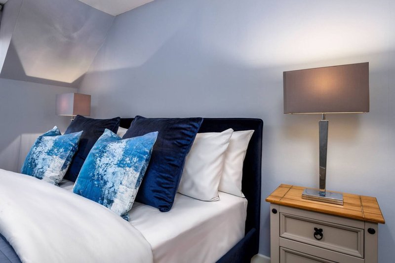 Modern bedroom with black bed frame, blue patterned pillows, white bedding and wooden nightstand with lamp