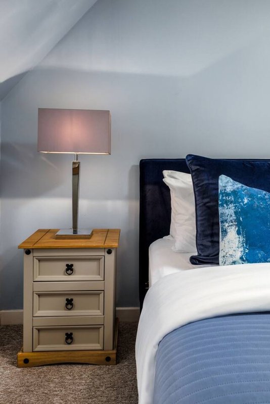 Bedroom with double bed, navy headboard, white pillows, bedside table lamp and wooden nightstand