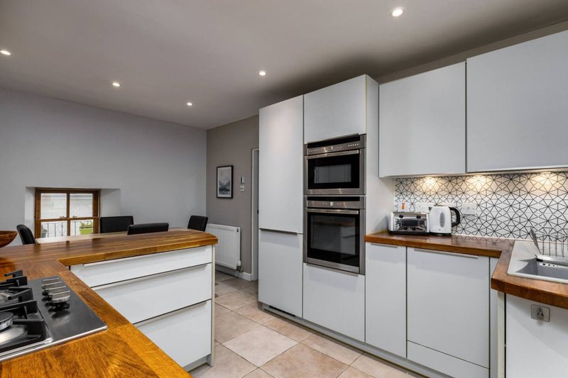 Modern kitchen with white cabinetry, wooden countertops, integrated appliances and tiled backsplash