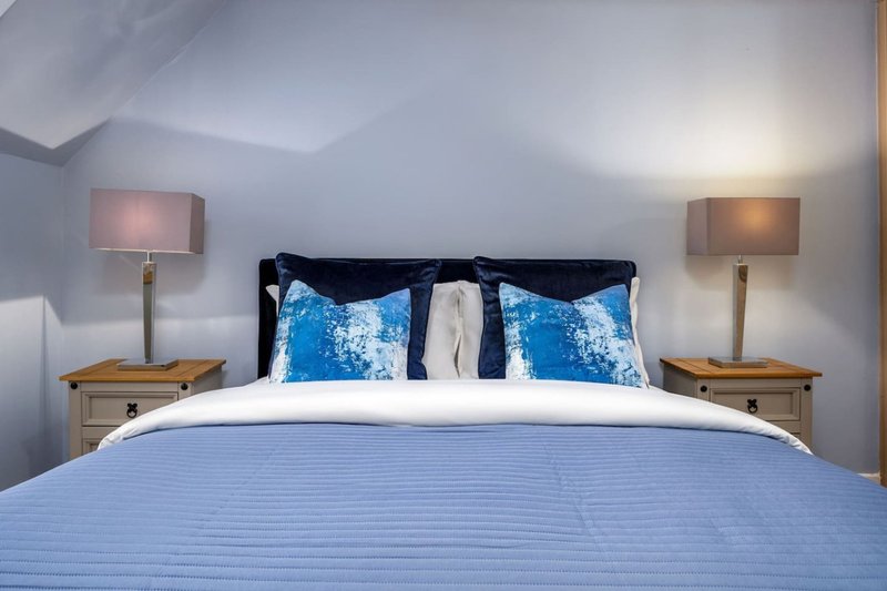 Modern bedroom with double bed, blue bedding, decorative pillows, wooden nightstands and table lamps