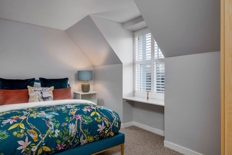 Attic bedroom with double bed, colorful duvet, bedside lamp and sloped ceiling