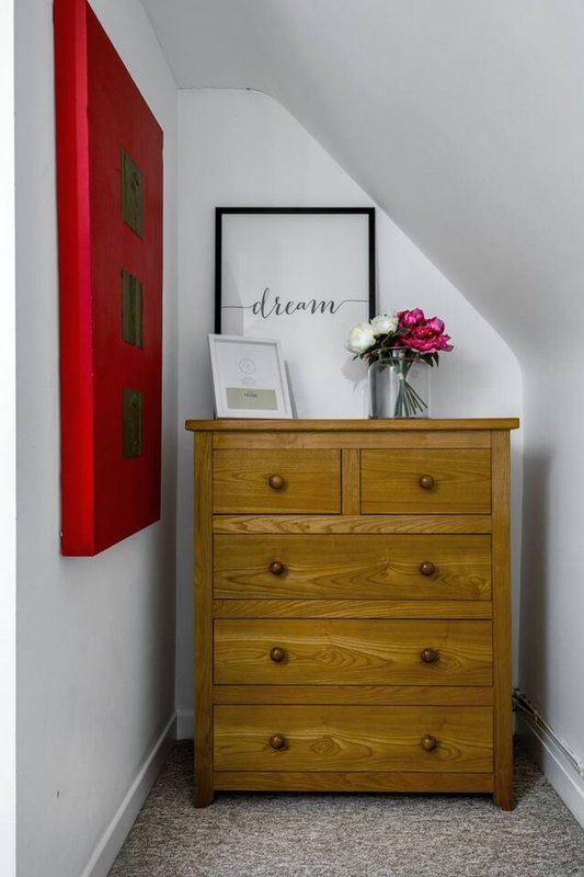 Wooden chest of drawers with framed artwork, flowers, and decorative items in bedroom alcove