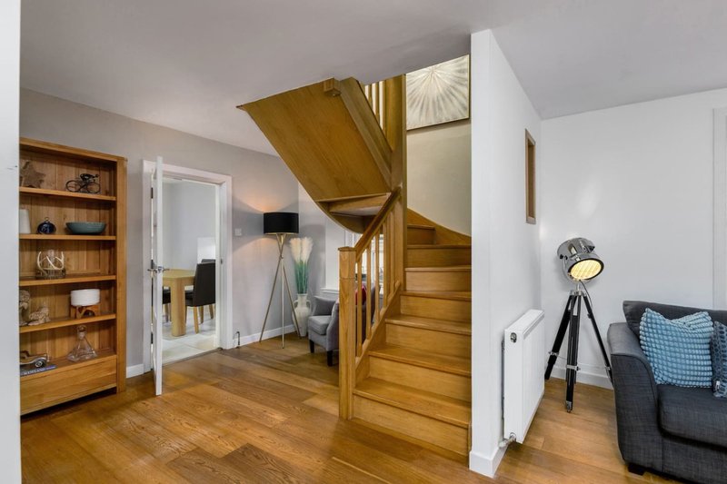 Open-plan living area with wooden staircase, shelving unit, sofa and lamp