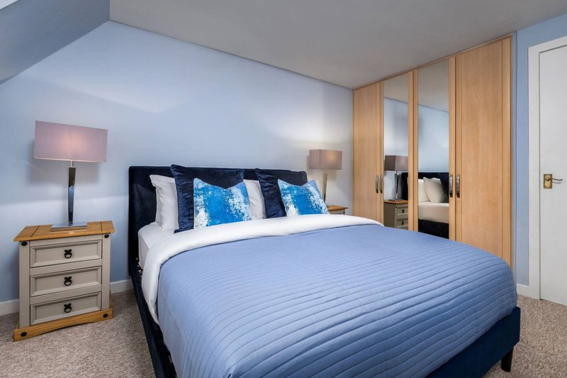 Modern bedroom with blue double bed, wooden wardrobe, bedside table and lamp