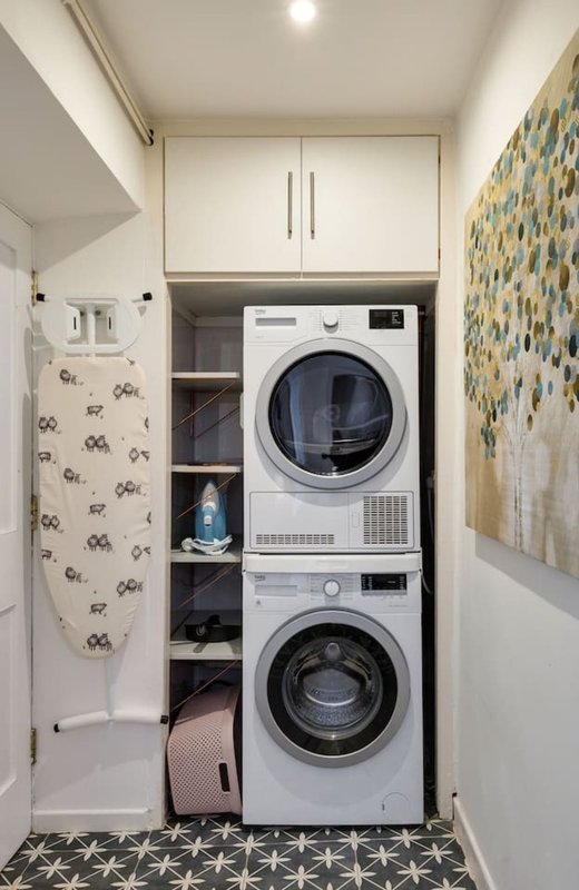 Compact laundry room with stacked washer and dryer, storage shelves, and patterned floor tiles