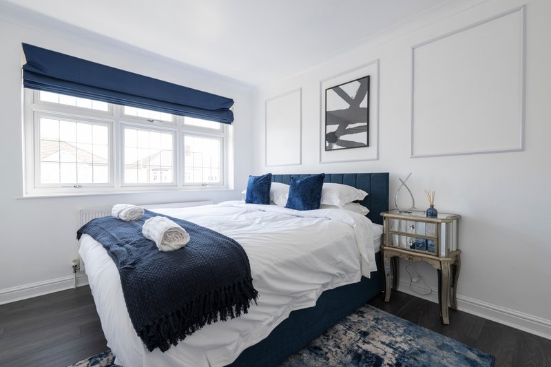 Bright bedroom with double bed, navy bedding, white walls, window with blue blind
