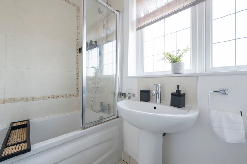 Bright modern bathroom with white pedestal sink, shower enclosure and window with plant