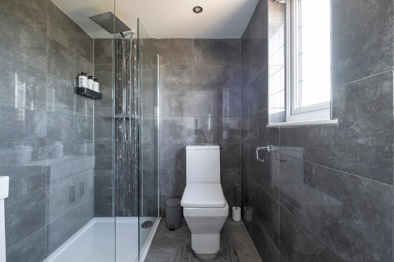 Modern bathroom with grey tile walls, walk-in shower, white toilet and window