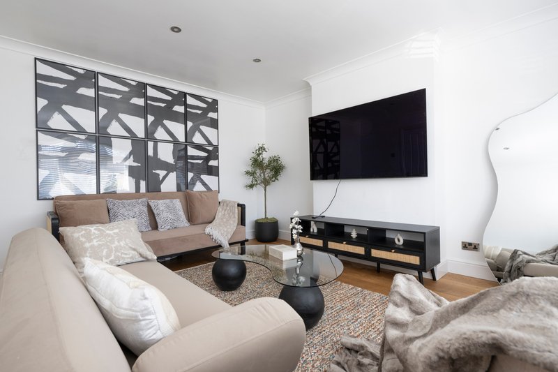 Modern living room with cream sofa, TV mounted on wall, wooden floor and decorative window panel