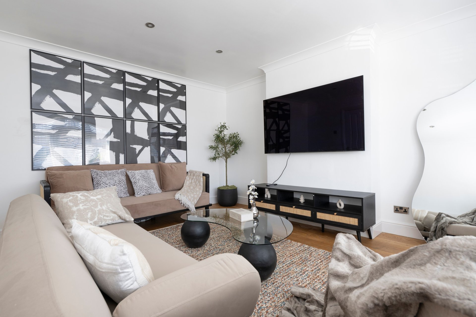 Modern living room with cream sofa, TV on wall, wooden floor and decorative window panels