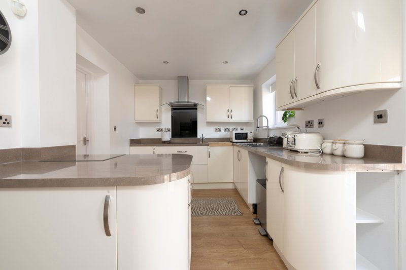 Modern white kitchen with gray countertops, island, stainless steel appliances and wooden flooring