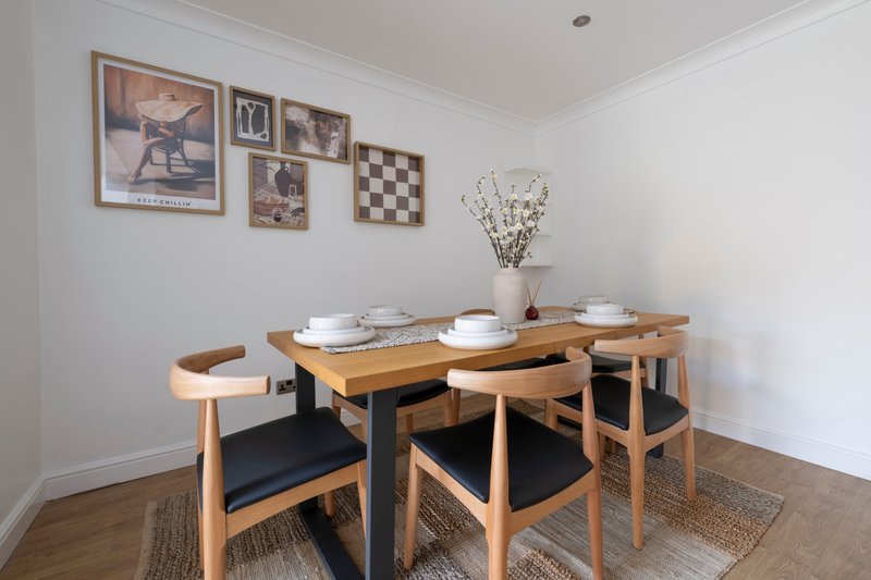 Dining room with wooden table, four chairs, place settings, framed wall art and flowers